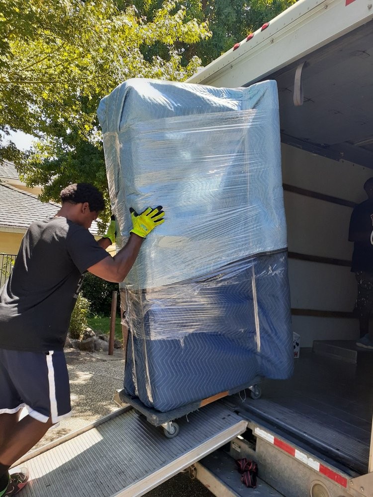 Professional movers transporting wrapped furniture down a ramp into a moving truck.