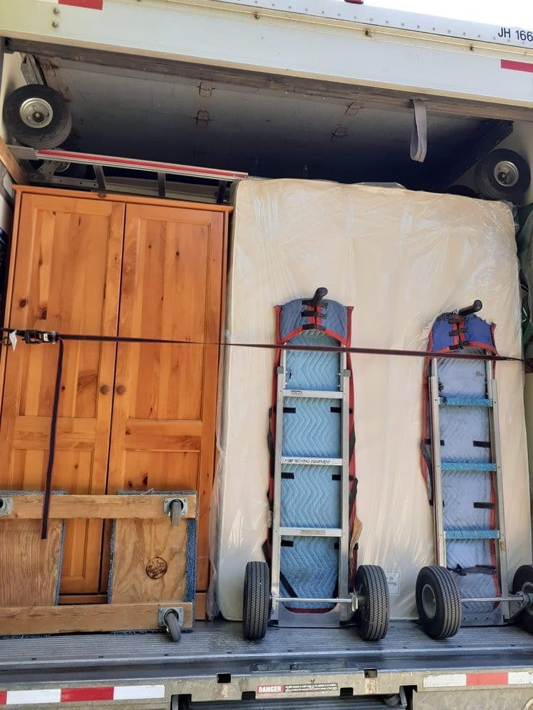 Wardrobe cabinet and mattress secured with straps on the back of a moving truck.