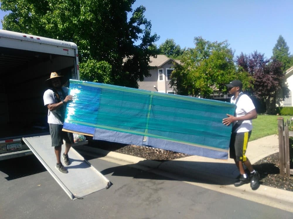 Professional movers in Sacramento carrying a fully wrapped sofa down a truck ramp.